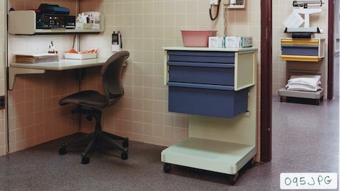Co/Struc L cart with a C-frame and blue drawers next to Action Office workstation with overhead storage, with Equa chair.