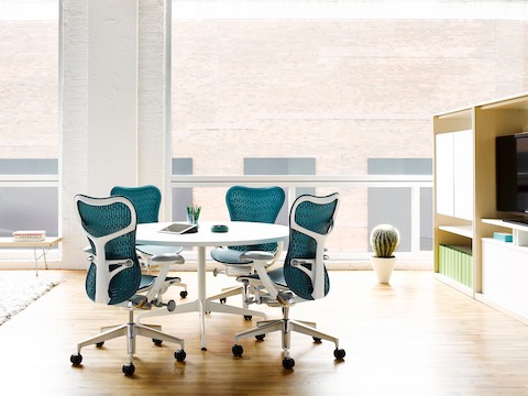 Four blue Mirra 2 office chairs surround a white Eames Table with a round top in an open meeting area.