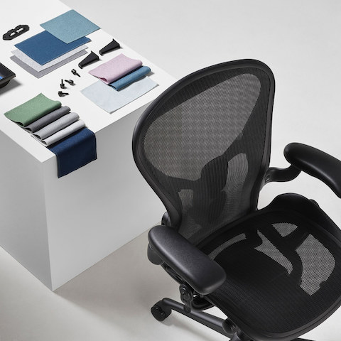 A black Aeron Office Chair with OE1 trolly plastic clips and Tu Pedestal Utility Tray, made from ocean-bound plastics, and Revenio textile swatches displayed on a cube.