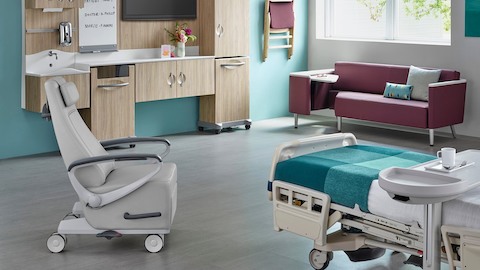 A patient room with a bed, recliner, guest sofa, and Compass System modular storage.