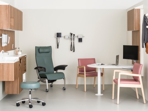 An exam room containing a patient recliner, caregiver stool, two side chairs, and wall-hung storage from the Compass System. 